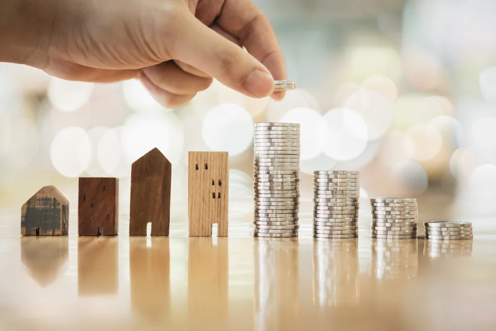 image of hand stacking coins opposite wooden houses, finding the most affordable places to live in Connecticut.